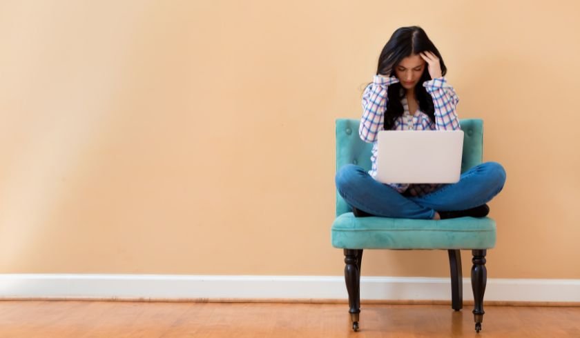 woman sitting cross-legged on a chair appearing to be stressed from working on a laptop 